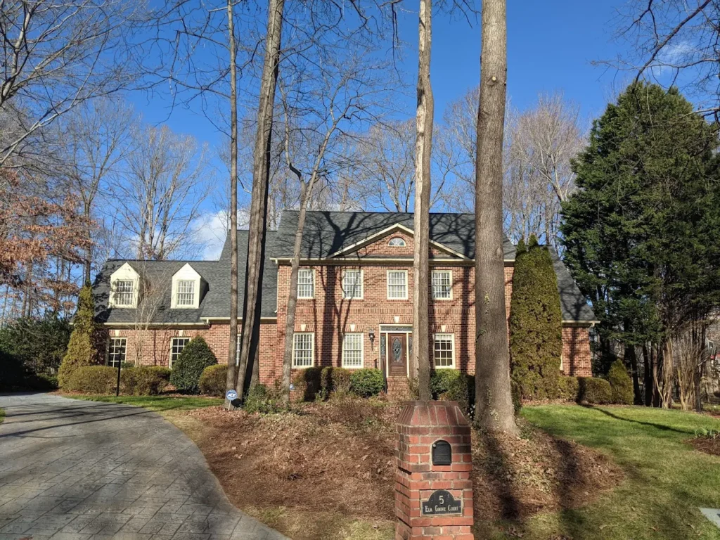 Mature trees in the front yard of a brick home in Greensboro NC serviced by JD TREE, LLC.